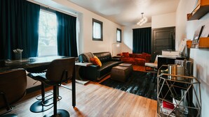A modern living room with a black leather sofa, a dining area with a table and chairs, and a kitchen area with a metal rack. - Swanky Speakeasy Stay-Hot Tub + Firepit-Minutes to Downtown (Moscow)
