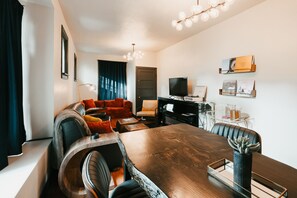 A modern living room with a wooden dining table, leather sofas, a TV, and a bookshelf. - Swanky Speakeasy Stay-Hot Tub + Firepit-Minutes to Downtown (Moscow)