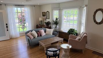 A living room with hardwood flooring, a grey sofa, a wooden coffee table, a round wicker side table, and a pink armchair.