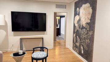 Un couloir avec un téléviseur à écran plat fixé au mur, une petite table avec une chaise et un grand tableau représentant des fleurs accroché au mur.