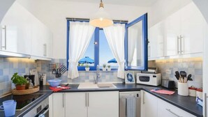 A modern kitchen with white cabinets, a black countertop, a built-in oven, a microwave, and a window with curtains. - Pool Villa Overlooking the Sea (Rhodes)