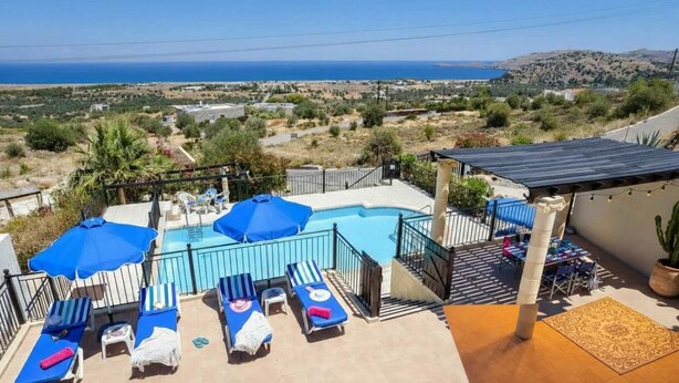 A pool area with lounge chairs and umbrellas, a view of the sea, and a hilly landscape in the background. - Pool Villa Overlooking the Sea (Rhodes)