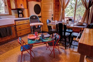 Uma cozinha acolhedora em estilo rústico, com armários de madeira, cafeteira e um espaço de jantar com mesa posta para dois.