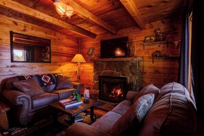 Un acogedor interior de cabaña de madera con chimenea, sofás de cuero, televisor y paredes de madera.