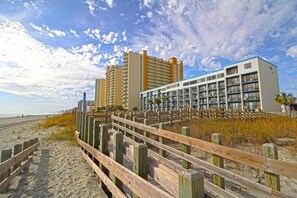 Ein Hotel direkt am Strand mit mehreren Hochhäusern, einer Holzpromenade und einem Sandstrand.