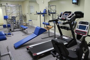 Ein Fitnessstudio mit Trainingsgeräten, darunter Laufbänder, eine Bank und Kraftgeräte.