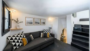 Ett modernt vardagsrum med en grå soffa, svartvita mönstrade kuddar, en liten växt och inramade tavlor på väggen.