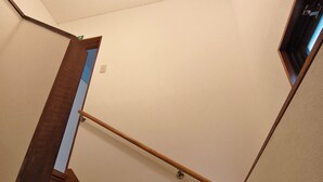 Eine Treppe mit Holzboden und Handlauf, die zu einer Empfangshalle mit Leuchte und Tür führt.