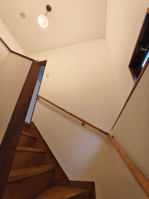 Eine Treppe mit Holzboden und Handlauf, die zu einer Empfangshalle mit Leuchte und Tür führt.