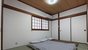 Ein traditioneller japanischer Raum mit Tatami-Böden, Futon-Bett, Schiebetüren und einem Fenster mit Gittermuster.
