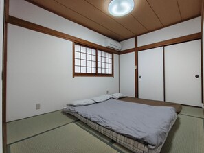 Ein traditioneller japanischer Raum mit Tatami-Böden, Futon-Bett, Schiebetüren und einem Fenster mit Gittermuster.