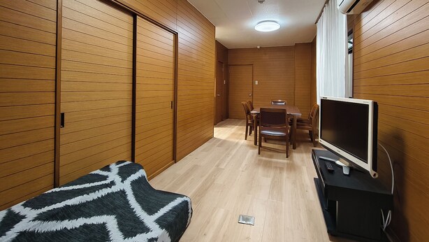 Ein kompakter Raum mit Holzwandverkleidung, einem Esstisch mit Stühlen, einer Couch und einem Fernseher auf einem Schrank.