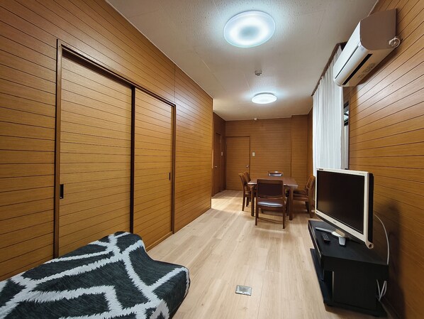 Ein kompakter Raum mit Holzwandverkleidung, einem Esstisch mit Stühlen, einer Couch und einem Fernseher auf einem Schrank.