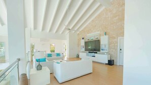 A spacious living area with a white sofa, a flat-screen TV, and a modern kitchen area. - 5BR Hispaniola Villa in Sosua (Sosúa)