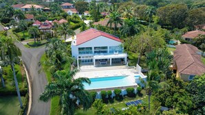 A modern house with a swimming pool, surrounded by lush greenery and palm trees. - 5BR Hispaniola Villa in Sosua (Sosúa)