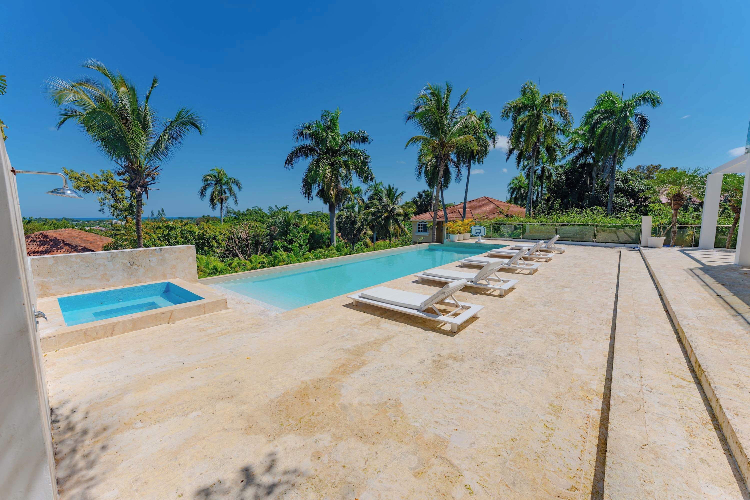A pool area with lounge chairs, a small hot tub, and palm trees.