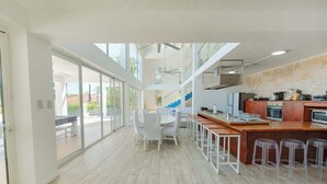 A modern kitchen with a central island, bar stools, and a view through large windows. - 5BR Hispaniola Villa in Sosua (Sosúa)