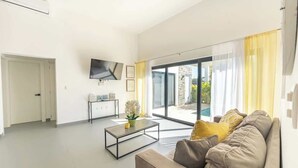 A modern living room with a sofa, a coffee table, and a flat-screen TV. There is a sliding glass door leading to an outdoor area. - Private Pool Villa in Sosua's Ocean Village (Sosúa)