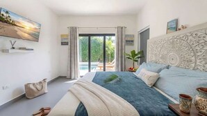 A bedroom with a bed, a view of the outdoors, a large window, and a decorative headboard. - Private Pool Villa in Sosua's Ocean Village (Sosúa)