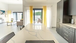 A modern kitchen with dark cabinets, a large island, and a dining area with a table and chairs. - Private Pool Villa in Sosua's Ocean Village (Sosúa)