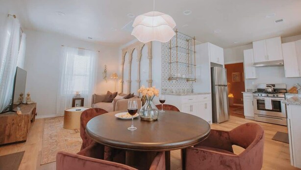 A modern kitchen with white cabinets, stainless steel appliances, and a dining area with a round table and chairs. - ZenDen Spa+Sauna+Hot Tub+Pet Friendly+No Pet Fee! (Albuquerque)