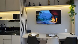A modern kitchen with a dining area, a flat-screen TV mounted on the wall, and a plant on the right. - Smart Bourbon 2009 (São Paulo)