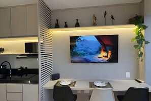 Eine moderne Küche mit Essbereich, einem an der Wand befestigten Flachbildfernseher und einer Pflanze rechts.