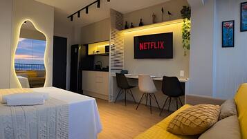 A modern hotel room with a bed, a desk, a chair, a TV, and a view of the cityscape.