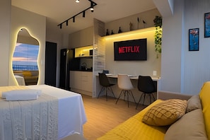 Habitación de hotel moderna con cama, escritorio, silla, televisor y vistas a la ciudad.