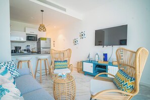 Ein modernes Wohnzimmer mit Rattanmöbeln, einem Flachbildfernseher und einer Küche im Hintergrund.
