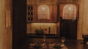 A dining area with a wooden table set for two, two wine glasses, and a kitchen in the background. - Private Jungle Retreat + Fast Wi-Fi & Private Pool (Tulum)