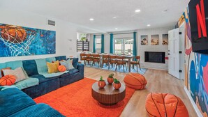 A living room with a blue sofa, orange rug, and a dining area with wooden chairs. - GAME ON! Heated Pool, Pickleball, Outdoor Theater! (Seminole)