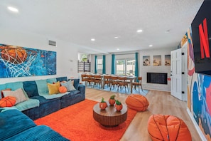 Ein Wohnzimmer mit einem blauen Sofa, einem orangefarbenen Teppich und einem Essbereich mit Holzsesseln.