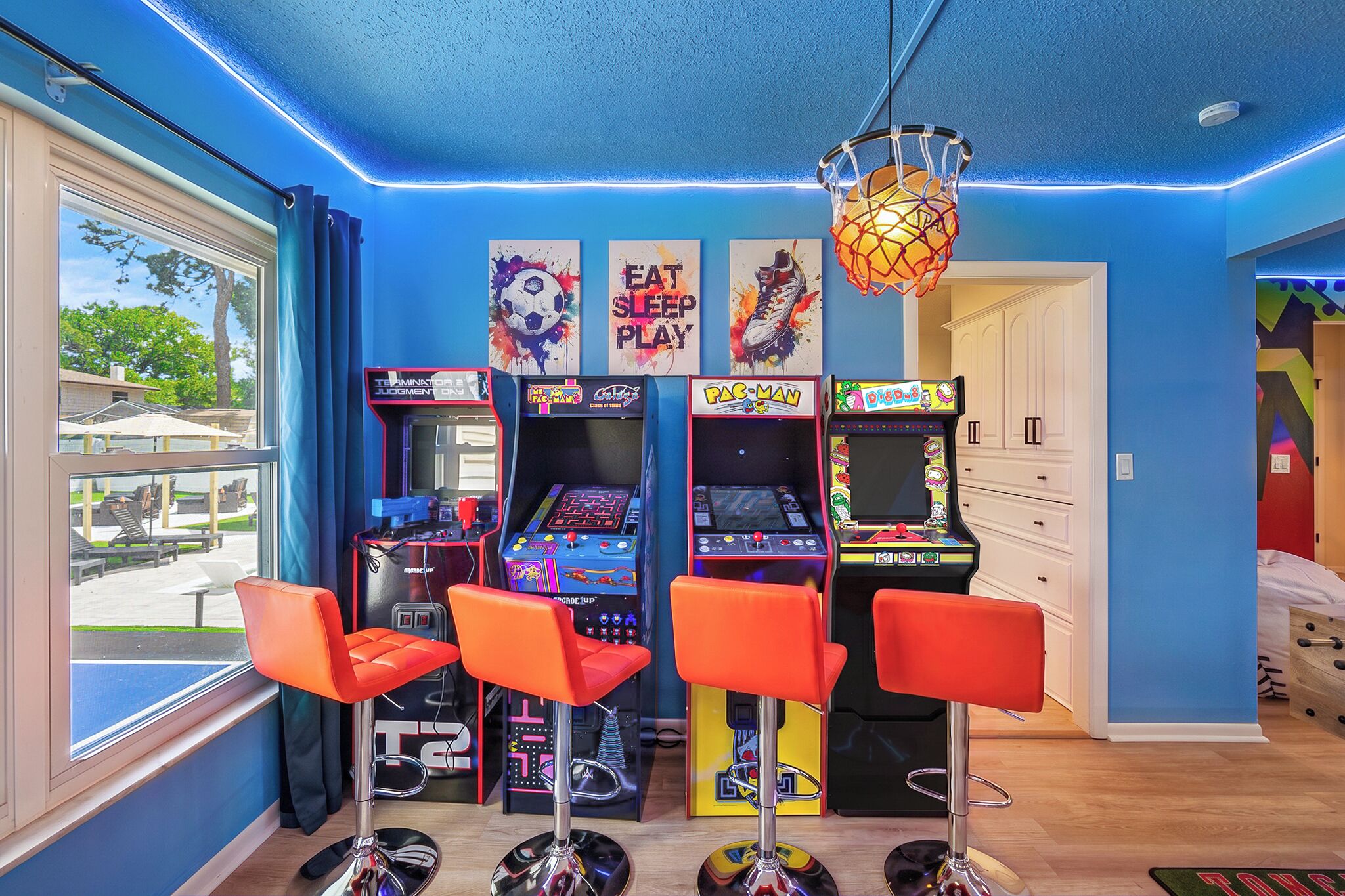 Um quarto com jogos de fliperama, banquetas vermelhas e uma cesta de basquete.