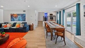 A modern living room with a sofa, coffee table, and orange accent pillows. A dining area with a table and chairs is visible. - GAME ON! Heated Pool, Pickleball, Outdoor Theater! (Seminole)