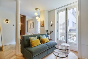 Ein modernes Wohnzimmer mit einem grünen Sofa, einem runden Couchtisch und einem großen Fenster mit Balkonblick.