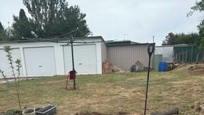 Un jardin à l’arrière de la maison, avec une terrasse en briques, des marches menant à une zone surélevée et un petit potager.