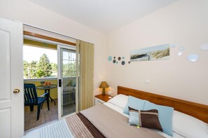 A hotel room with a bed, a nightstand, a lamp, a painting, and a view of the outdoors. - Beachfront Apartment Mareo 6 (Nin)