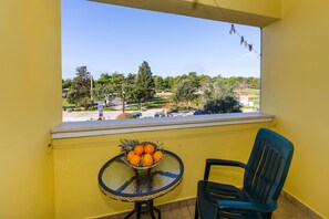 A balcony with a table holding oranges and a chair, overlooking a green landscape with trees and a road. - Beachfront Apartment Mareo 6 (Nin)