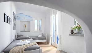 A modern bedroom with a bed, a small seating area, a window with curtains, and a wall-mounted shelf with plants. - Panormos Retreat With Pool (Mykonos)