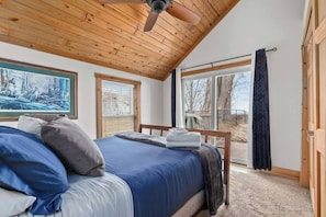 Ein Schlafzimmer mit Bett, Deckenventilator, Fenster mit Jalousien und einer Tür, die nach draußen führt.