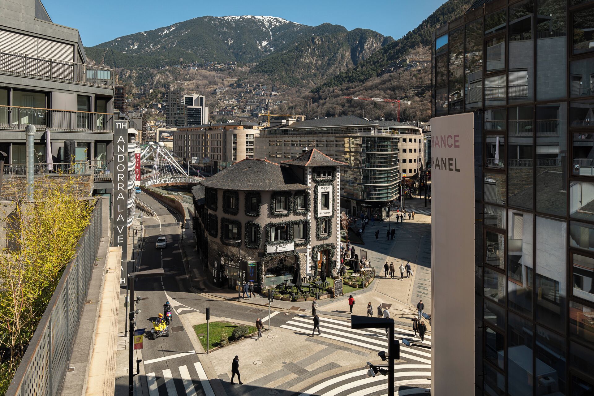Un paisaje urbano con un edificio destacado que tiene un letrero de restaurante, un paso de peatones y un teleférico al fondo.