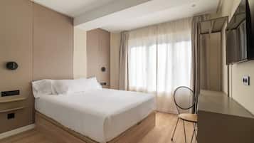 Una habitación de hotel con una cama, una silla, un televisor y un ventanal con cortinas.