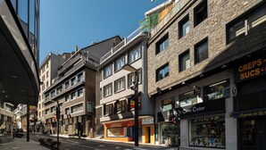 Vista de la calle con edificios de varios pisos, locales comerciales y un paso de peatones.