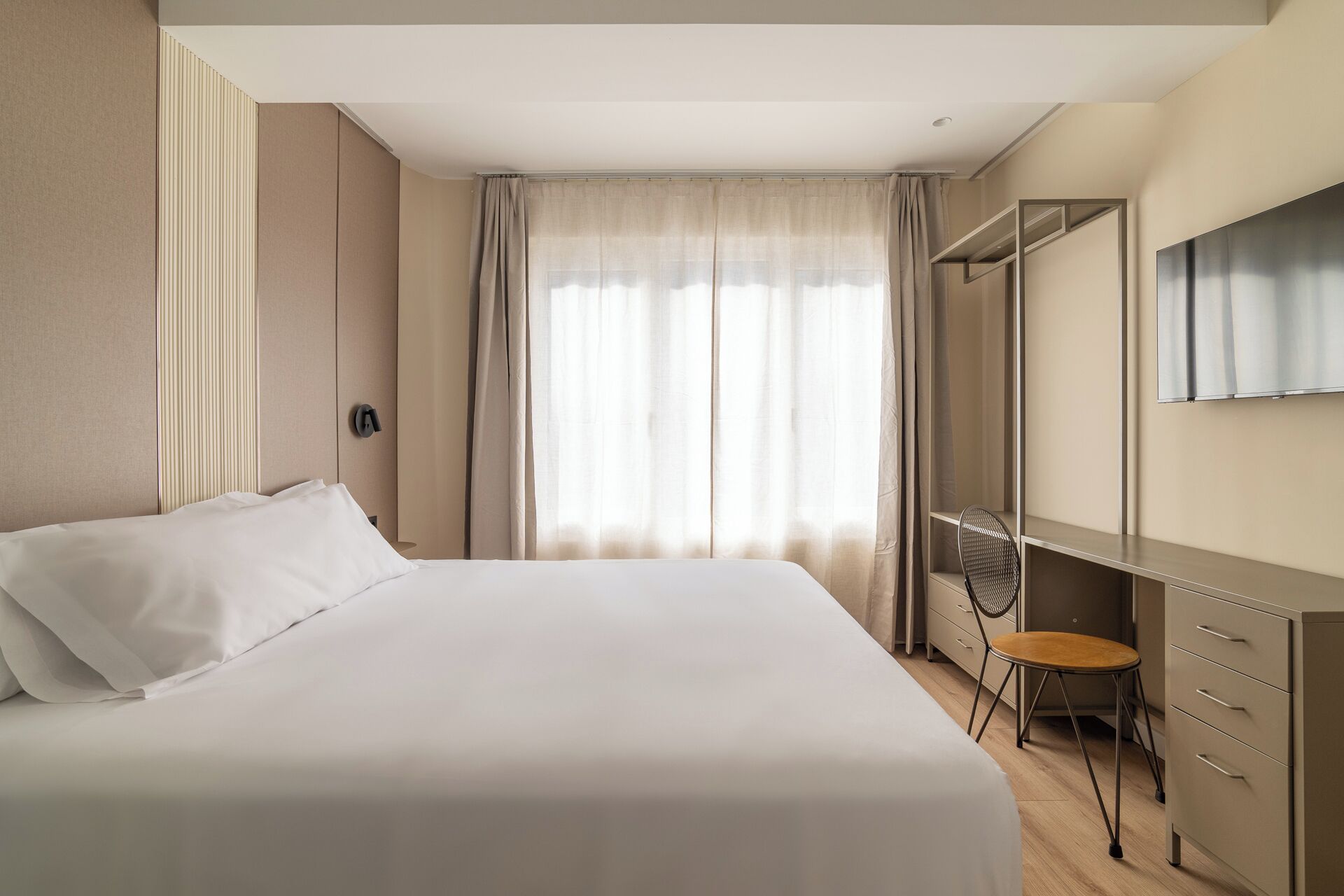 Una habitación de hotel con cama, escritorio, silla, espejo y ventana con cortinas.