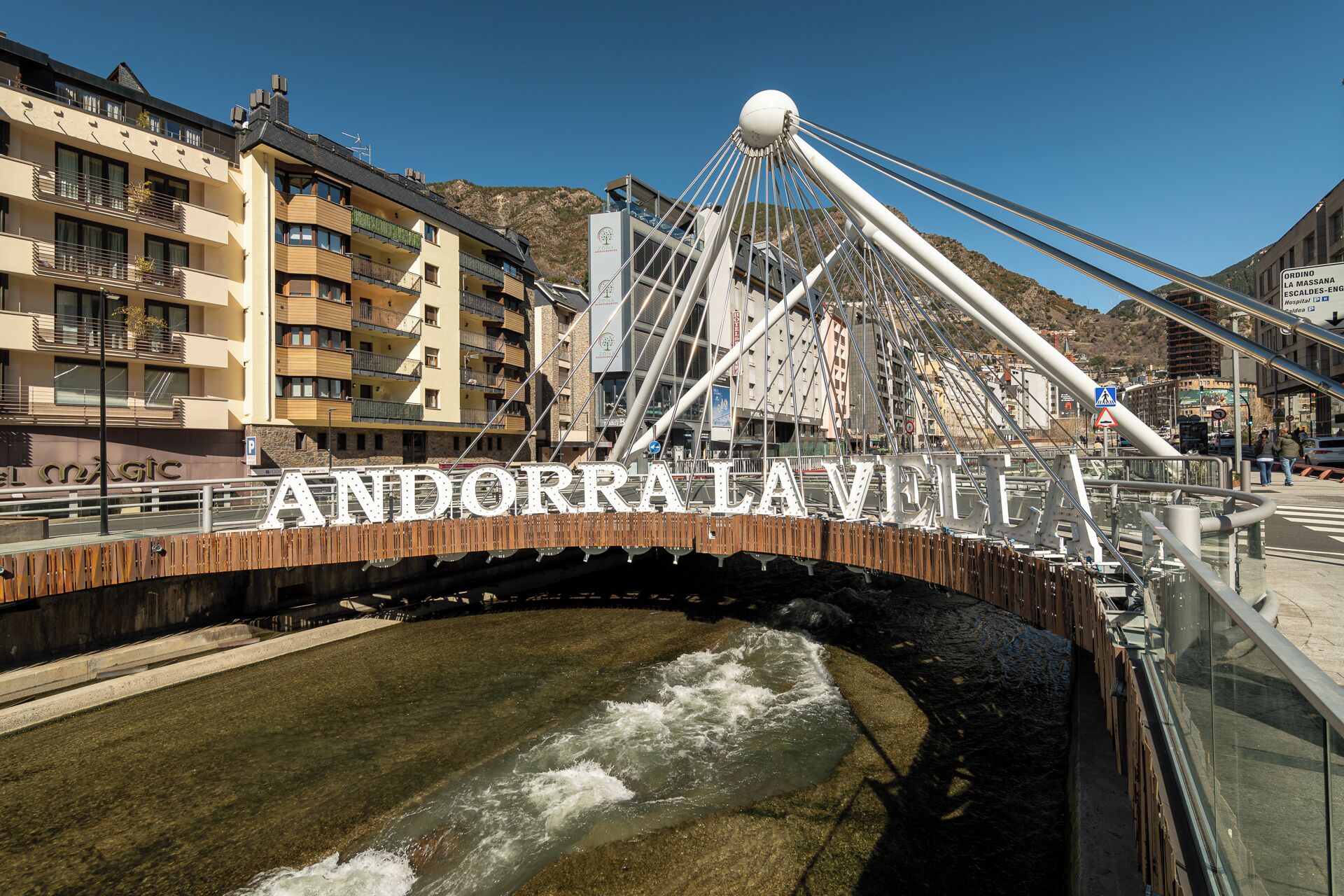 A bridge with the name 'Andorra la Vella' prominently displayed, a mountainous backdrop, and a body of water below.