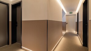 Un pasillo moderno de hotel con piso alfombrado, luces empotradas y puertas de marco oscuro.