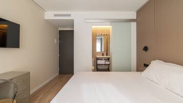 A hotel room with a bed, a desk, a chair, a bathroom with a sink and mirror, and a television on the wall.