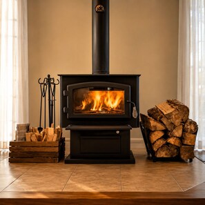 A wood-burning stove with a glass front, a stack of firewood, and a metal rack with logs. - Chalet du Sommet SPA (Sainte-Béatrix)
