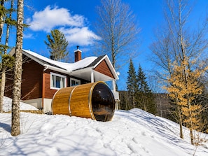 A cabin with a wooden barrel, snow-covered roof, and a clear blue sky. - Chalet du Sommet SPA (Sainte-Béatrix)
